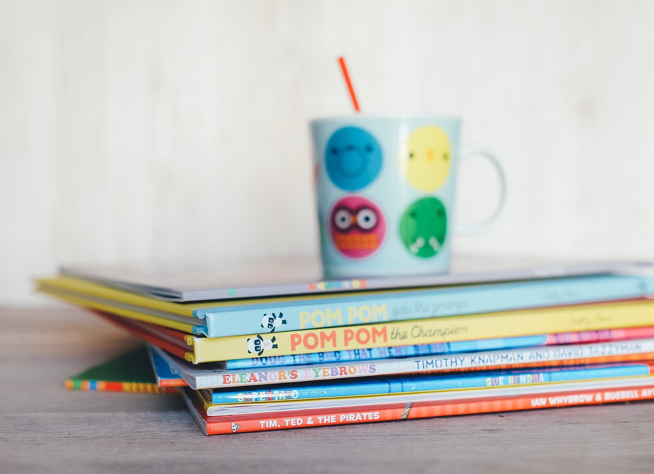 A stack of colourful young children's books with a cup and straw placed on top