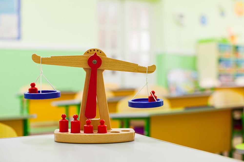 Close view of wooden scales with weights placed on table with white surface. Lessons topic visual demonstration. Empty classrom on a background