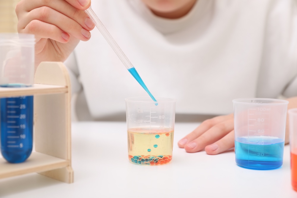 Girl mixing colorful liquids at white table indoors, closeup. Chemical experiment set for kids