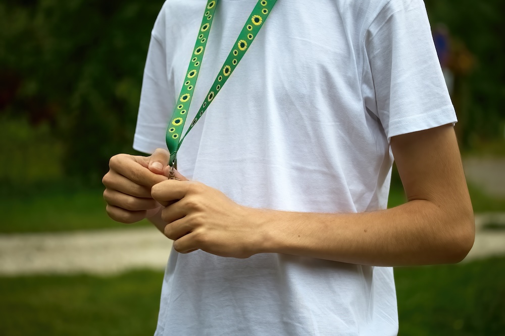 Sunflower lanyard, symbol of people with invisible or hidden disabilities. A person wearing a white shirt fiddles with a green lanyard adorned with sunflower designs.