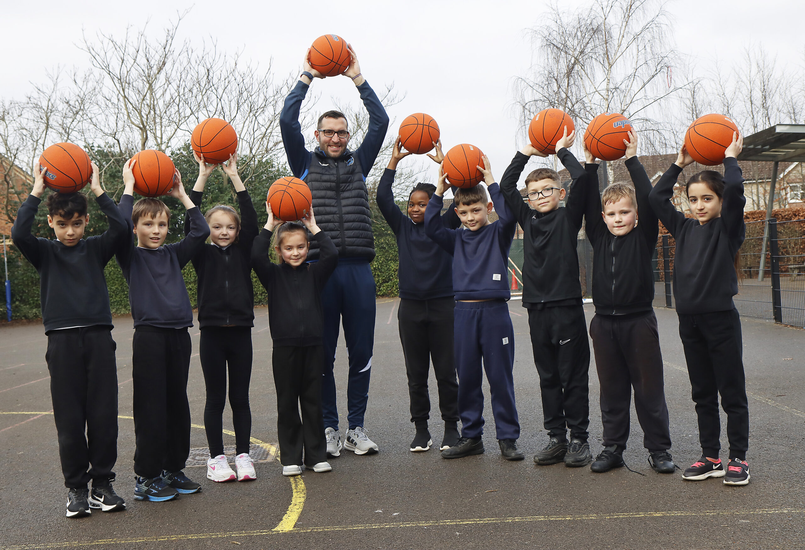Piper's Vale children and teacher holding basketballs in the air in the playground